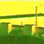 A.P. ASTRA - Cross: A coastal industrial facility with five tall chimneys or towers, positioned near the water with a breakwater structure in the background, under a yellow-green tinted light.