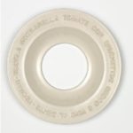 A white, round plate with a wide rim and a hollow center. Inspired by Martin Kippenberger - Italienischer Teller (italian plate), Italian words like "MOZZARELLA," "TOMATE," and "SPAGHETTI" are embossed around the rim.