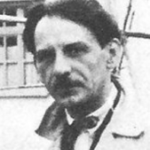 Schwarz-Weiß-Foto von Georgios Bouzianis, einem Mann mit dunklem Haar und Schnurrbart, der einen hellen Mantel über einem Hemd und einer Krawatte trägt und mit neutraler Miene in die Kamera schaut. Der Hintergrund scheint ein Außenbereich zu sein.