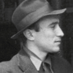 Schwarz-Weiß-Profilfoto von Giannis Moralis, der einen Filzhut und eine Anzugsjacke trägt und mit einem neutralen Gesichtsausdruck nach rechts schaut.