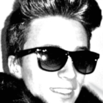 Black and white photo of Leon Fontana with short, styled hair, wearing large dark sunglasses and a fur or fluffy collar, smiling and facing slightly to the right.